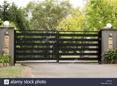 عکس - دروازه های ورودی راهروی فلزی در حصار آجری و در پس زمینه درختان باغ
