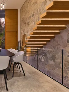 طراحی مدرن خانه.  دیوار سنگی.  پلکان چوبی شناور.  کف مرمر.  میز ناهار خوری چوبی تیره.