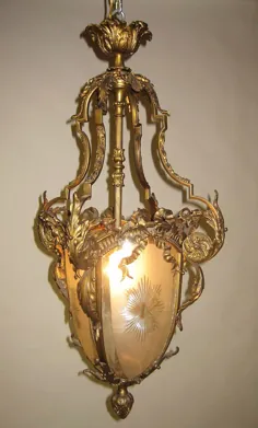 یک فانوس شیشه ای مروارید برنز و الماس برش خورده - شیشه ای گلابی XV قرن بیستم قرن بیستم بسیار زیبا.  بدنه برنز طلای بیضوی با یک چراغ منفرد ، با سه صفحه شیشه ای متمرکز با طرح آفتاب سوزی.  بدنه برنز طلاکاری شده طومار با طومارها ، آکانتوس ، گل سرخ و برگها ، هر تخته با تاج ها و روبان های برنز طلا طوسی ، پایین تزئین شده با یک بلوط ، پاریس ، حدود 1890-1900