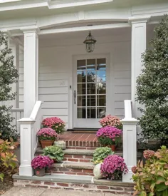ایوان جلوی سرپوشیده ، درب ورودی سفید ، سایدینگ سفید ، پله های آجر قرمز ، گیاهان ، ستون های مربع شکل.