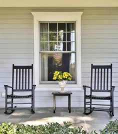 ایوان جلویی با صندلی های گهواره ای مشکی و میز با گل های زرد و گلدان سفید ، سایدینگ خاکستری.