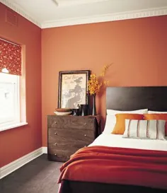 اتاق خواب نارنجی با سقف سفید و مبلمان چوبی تیره بالشهای نارنجی ملافه سفید